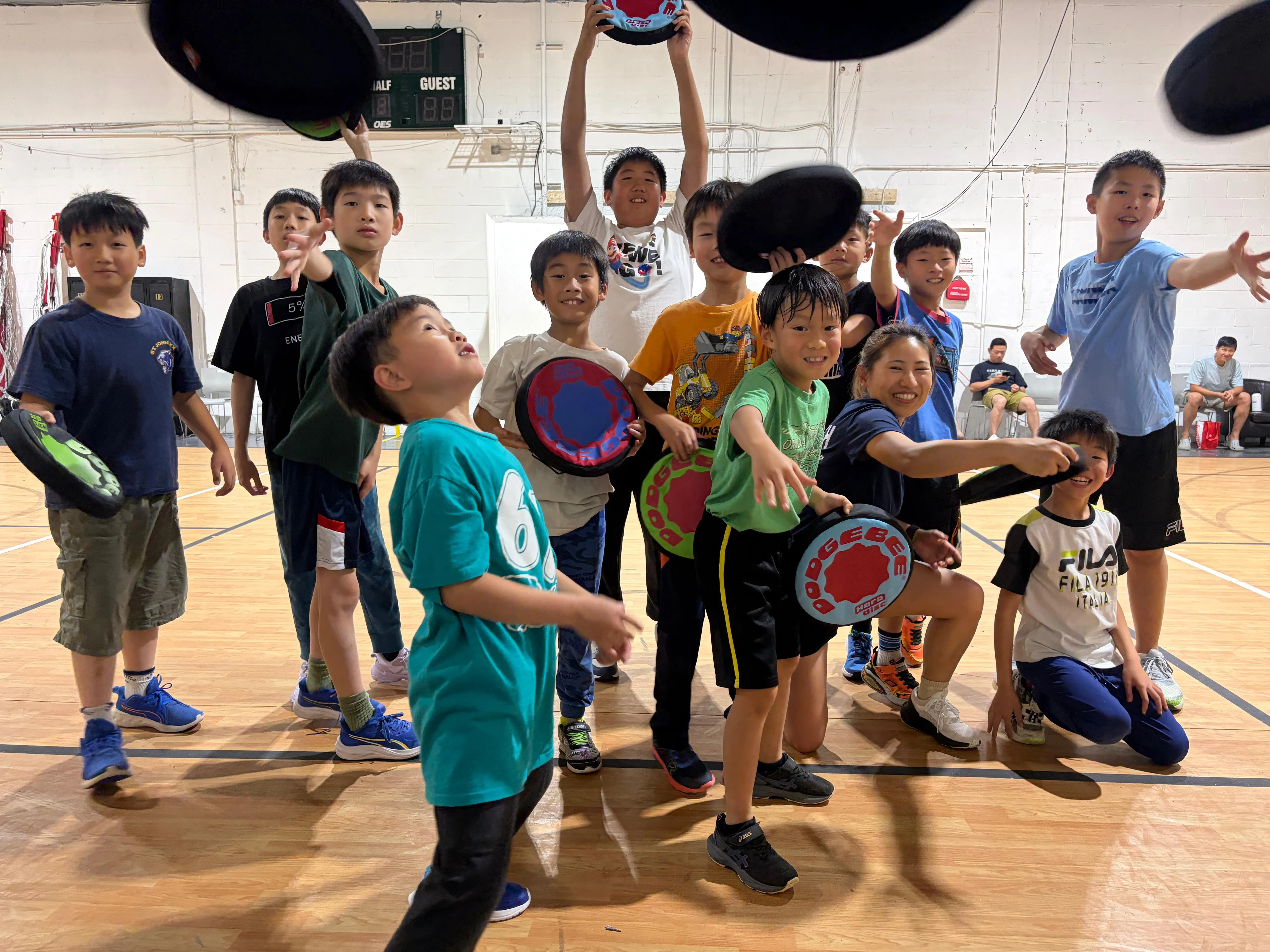 Young Dodgebee players and their coach celebrate together on an indoor court.